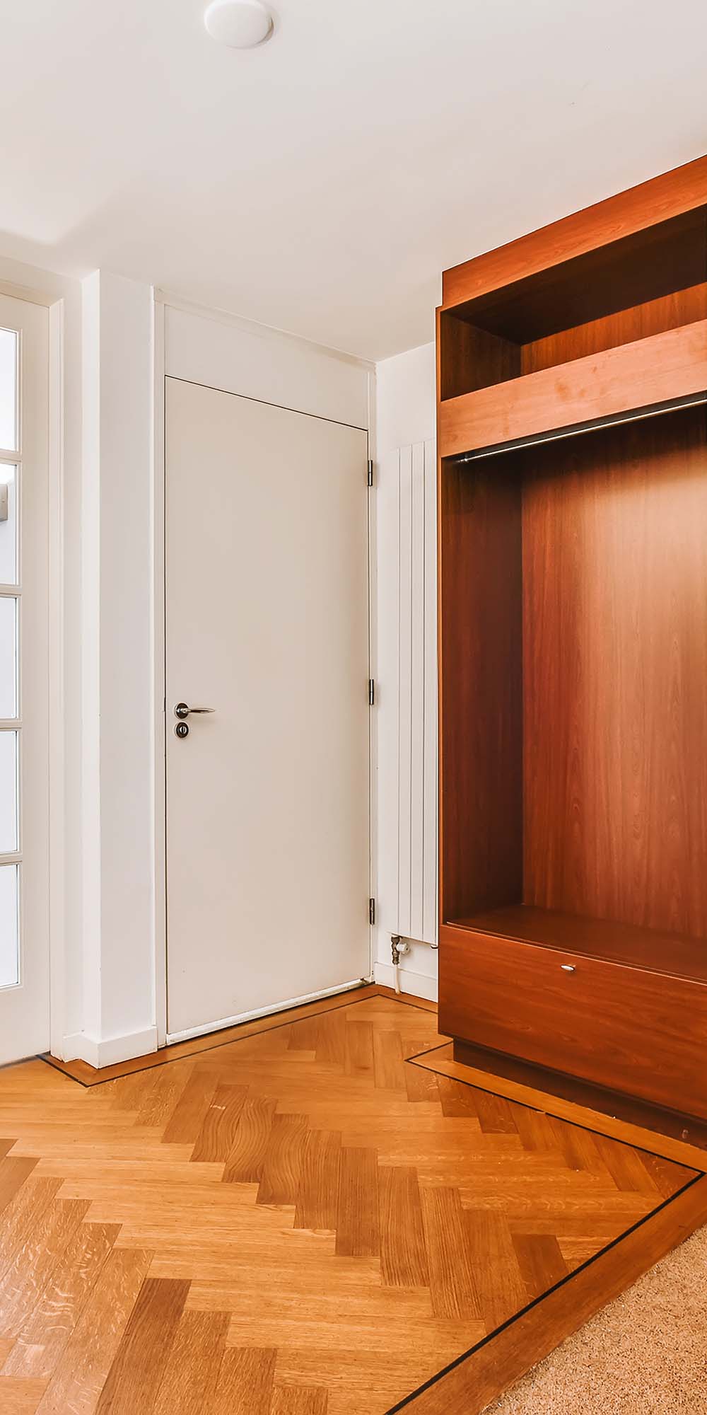 White interior door beside open wooden wardrobe on herringbone floor